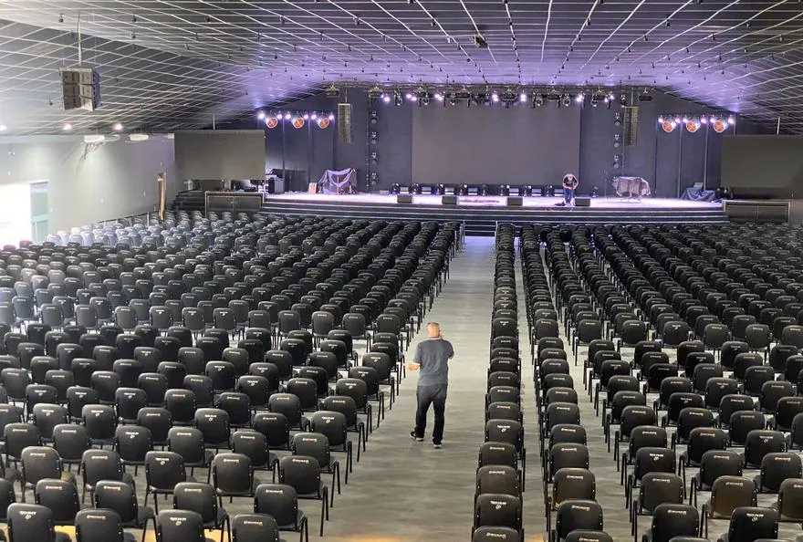 Auditório de grande porte com palco, estrutura de iluminação e cadeiras instaladas